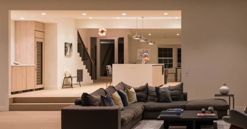 Living room with dark couch and hanging lights with kitchen in background