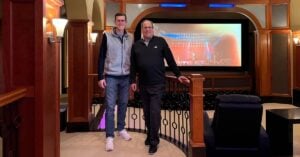 Brian Wiersma and Mike Major stand in a home theater room with sconce lighting on the left and a screen TV in the back
