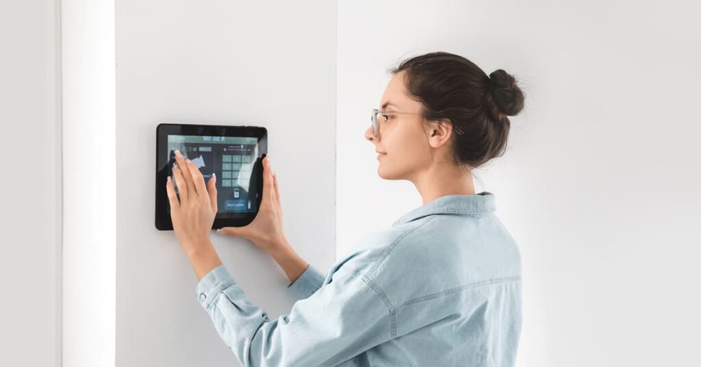Woman with eyeglasses using a LCD screen on the wall to view home security