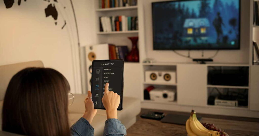 Person sitting on a couch in the living room using a tablet PC to control a smart flat screen TV on the wall