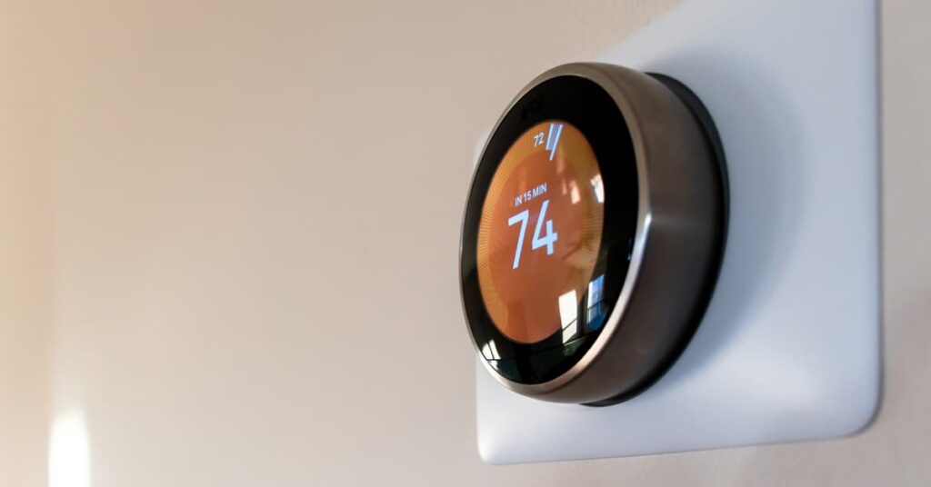 Circular Smart HVAC thermometer with orange LCD background on a wall