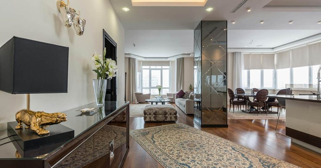 Well lit home interior with table and chairs, sofa and lounge chair with lamp on cabinet.