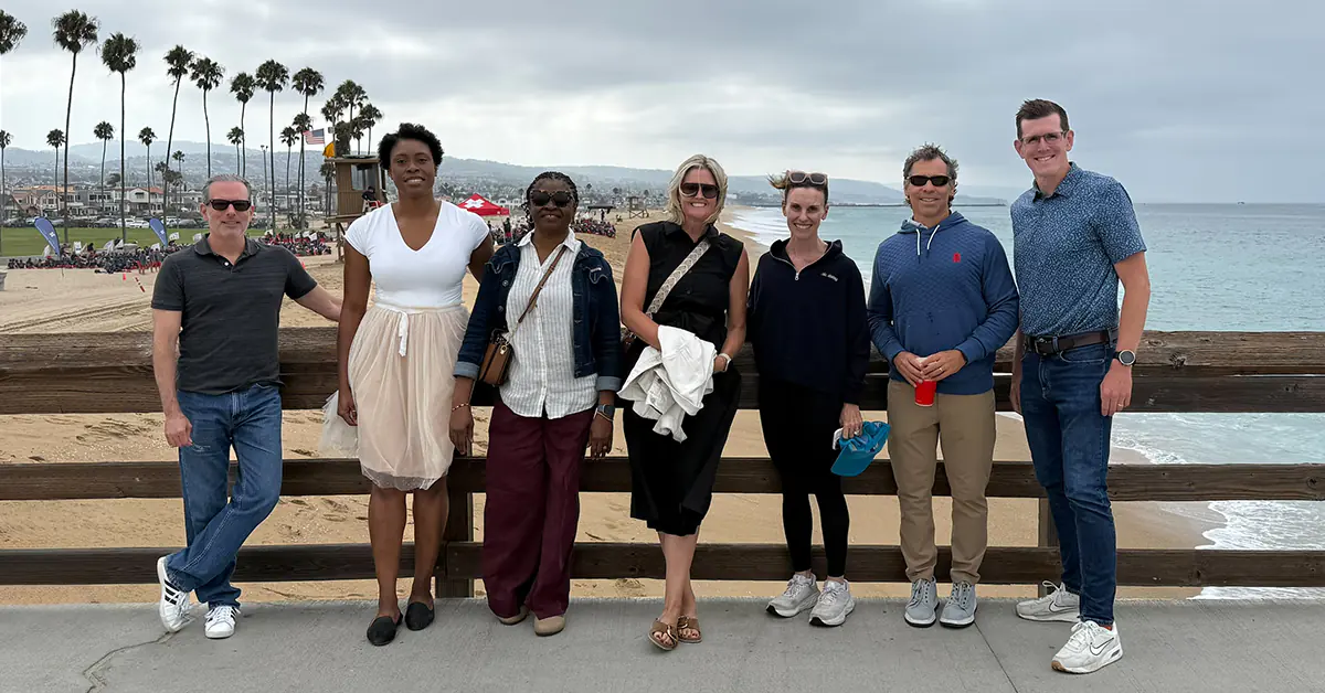 Pictured from left to right, are: Steve Gottlieb, Awele Nwaeze, Ijeoma Nwaeze, Tracy Purdy, Hagan Kappler, Joe Thomas, and Brian Wiersma standing on boardwalk near a beach with palm trees in the background