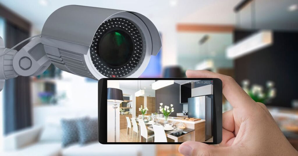 Security camera on the wall with a person holding a smart phone in front of it with the video feed from the camera on it