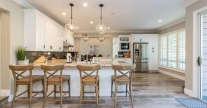 Kitchen area with light colored walls and an eating island with four chairs and several hanging lights