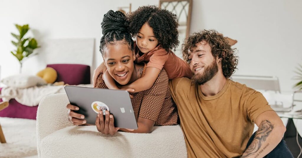 family of three sitting on their living room sofa with tablet