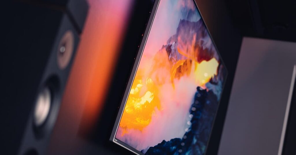 Flat screen TV on wall with a colorful image on it and a home speaker next to it