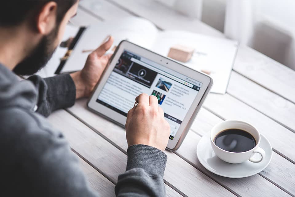 Over the shoulder view of a man sitting at a table using a tablet PC with a cup of coffee on the table