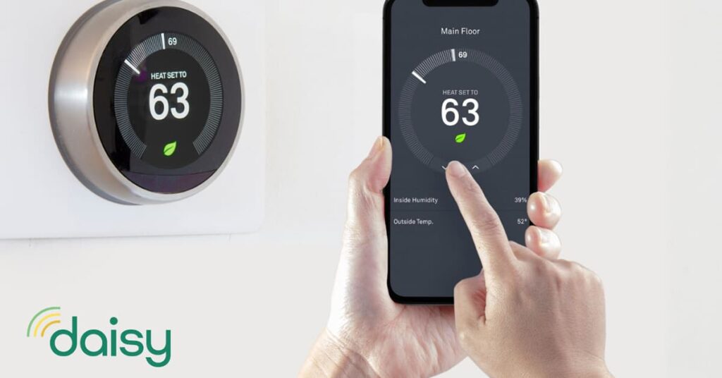 Smart thermostat on the wall and a person holding a smartphone with a smart thermostat temperature control app on the screen