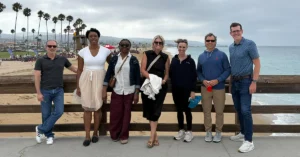 Pictured from left to right, are: Steve Gottlieb, Awele Nwaeze, Ijeoma Nwaeze, Tracy Purdy, Hagan Kappler, Joe Thomas, and Brian Wiersma standing on boardwalk near a beach with palm trees in the background