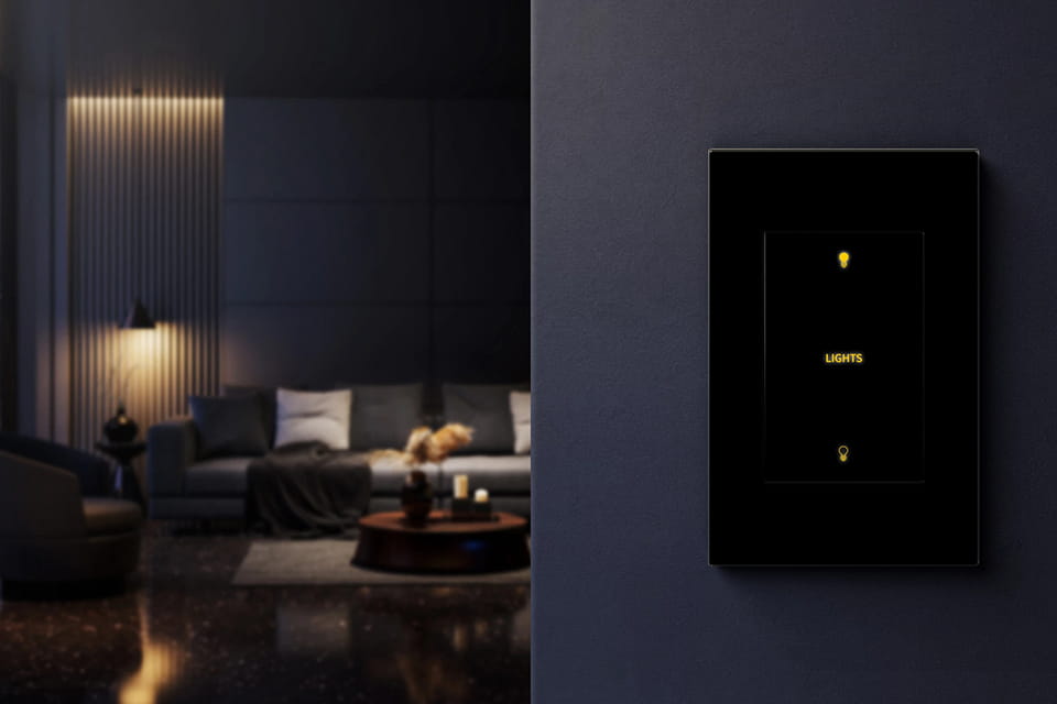 Darkened room at night with a couch and lounge chair in the background with a light control switch in the foreground on a wall
