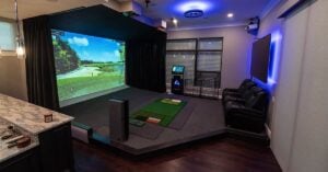 Game room with a golf simulator machine including two lounge chairs and a flat screen TV on the wall.