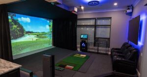 Game room with a golf simulator machine including two lounge chairs and a flat screen TV on the wall