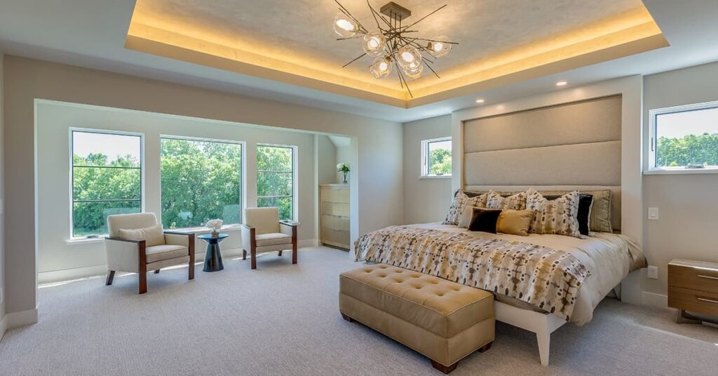 Light colored bedroom with good lighting and two chairs in front of a window to the left
