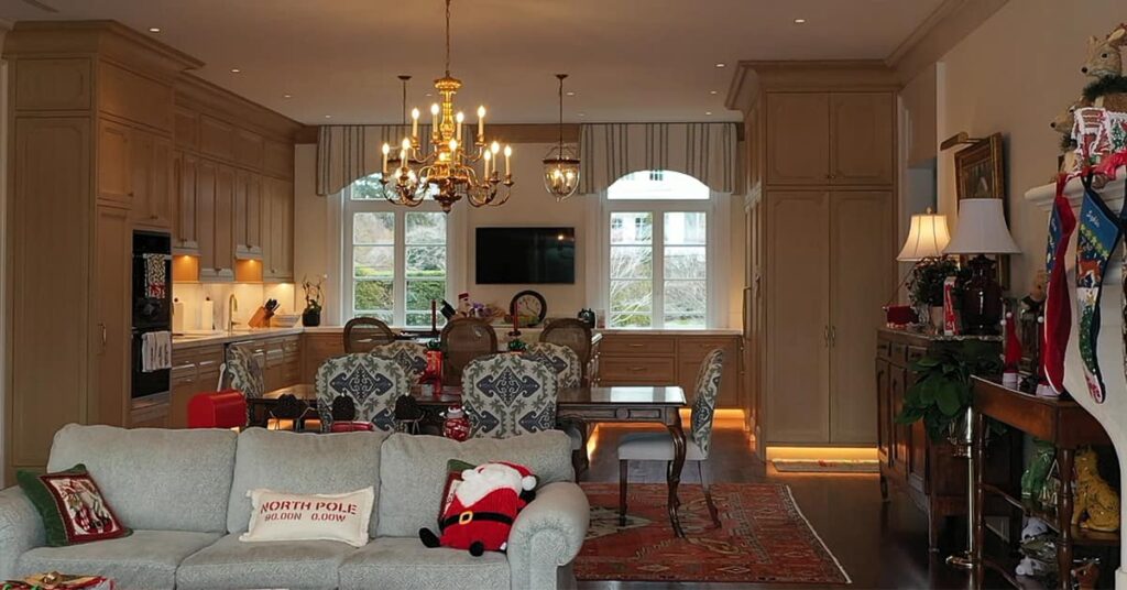 Living area with white couch and dinner table with kitchen in the back and holiday decorations on the walls