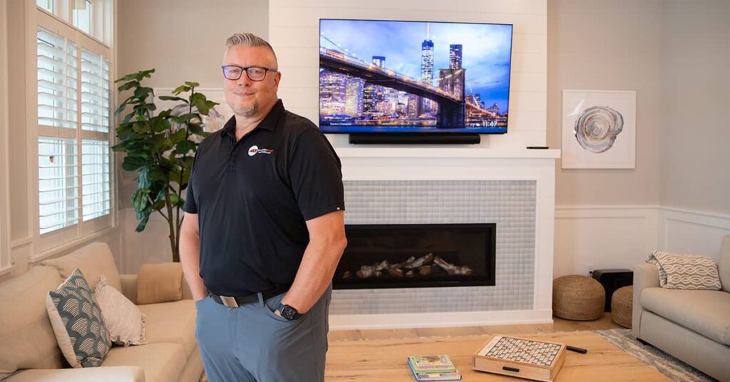 Peter Cook from Daisy Kalamazoo standing in a living area in front of a fireplace and a flat screen TV on the wall