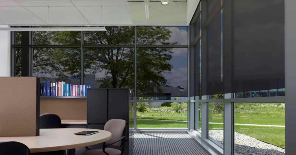 Office interior with a round table and chairs to the left and glass walls with smart shades half drawn