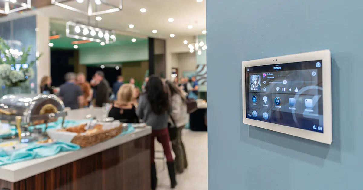 Tablet control pad on the wall with a kitchen and people celebrating to the left