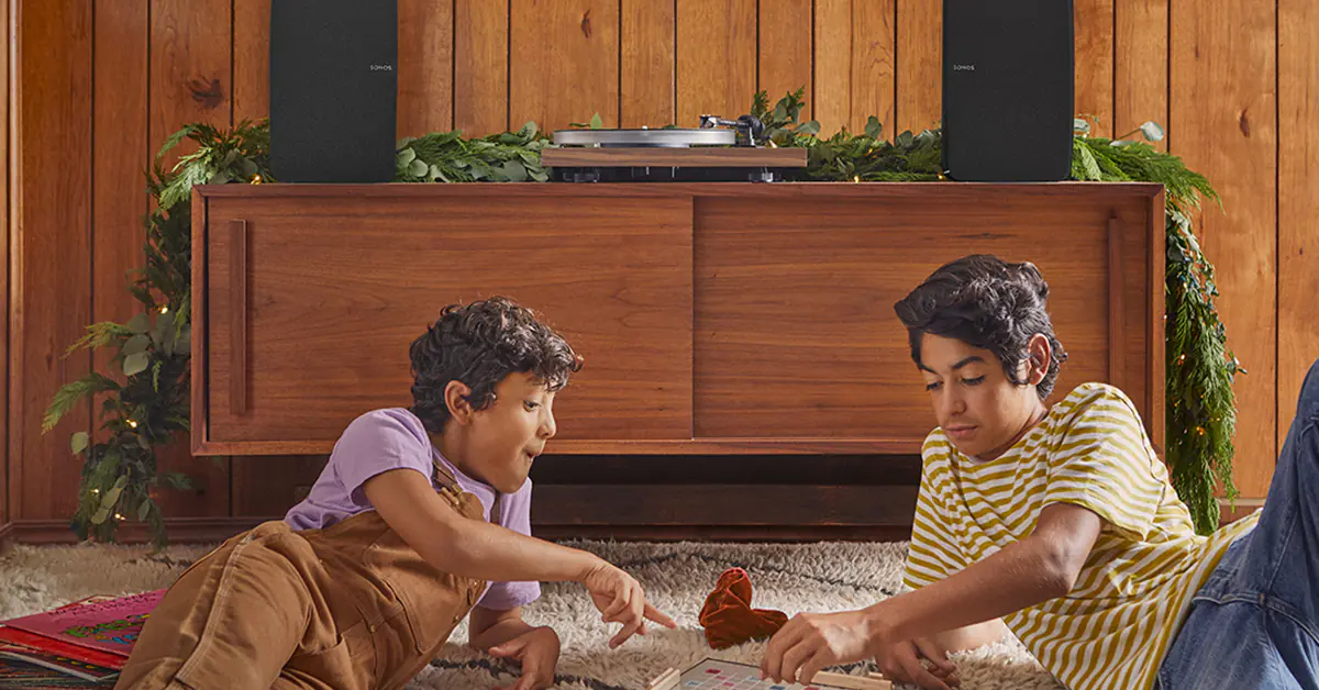 Two boys playing a game on the floor in front of a wooden cabinet with a record player on top of it